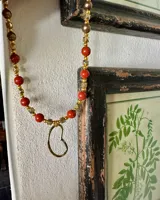 Collar con cuentas de piedra color terracota, cuentas doradas y dije colgante con forma de corazón.