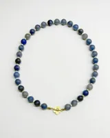 Collar de cuentas esféricas en tonos azules y grises, con cierre marinero frontal de metal dorado en forma de flor.