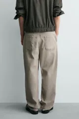 Pantalón de corte relajado confeccionado en tejido de algodón con efecto lavado. Presenta diseño de cinco bolsillos, cierre frontal con cremallera y botón, y detalles de estampados a contraste en la parte delantera y trasera.