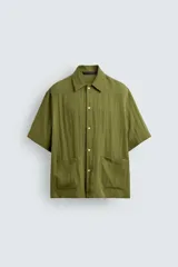 Camisa de corte relajado confeccionada en tejido fluido de lyocell y viscosa, color verde oliva. Presenta cuello solapa, manga corta, cierre frontal de botones y dos bolsillos plastrón en la parte inferior.
