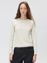 Remera de manga larga con cuello a la base, confeccionada en tejido de punto acanalado color beige. Presenta un logo bordado en el centro del pecho.