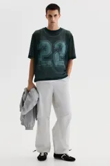 Remera de malla color verde oscuro, de corte oversized y manga corta, con cuello redondo y gran estampado frontal con el número 22 en tono celeste.