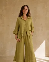 Camisa verde pistacho de lino, con cuello camisero, cierre frontal con botones y mangas tres cuartos con volados escalonados en los puños y en el ruedo asimétrico.
