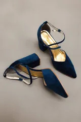 Zapato de taco alto azul oscuro, confeccionado en gamuza, con diseño de punta fina, escote en V y tiras cruzadas en diagonal con hebilla ajustable en el tobillo.