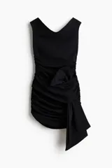 Vestido corto negro en punto texturizado, de corte entallado con hombros descubiertos, escote en V y frunces laterales que generan un efecto drapeado. Cuenta con un nudo ancho asimétrico al frente.