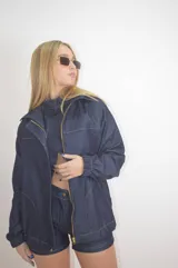 Campera de jean azul con cierre dorado, cuello clásico, mangas largas con puños elásticos y costuras blancas a contraste.