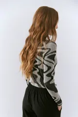 Polera de tejido de punto con diseño vanizado que combina tonos tierra y crema en un patrón abstracto de líneas onduladas. Presenta cuello alto, mangas largas y un ajuste entallado al cuerpo.
