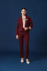 Pantalon de vestir color verde oscuro, de corte recto y tiro alto. Presenta dos solapas decorativas en la cintura con apliques de broches metálicos con forma de insectos.