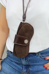 Estuche para lentes de gamuza color chocolate, con correa larga para colgar al cuello y cierre frontal con solapa de cuero liso y botón metálico.