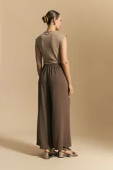 Pantalón ancho color tostado, de silueta fluida y cintura elastizada. Presenta una pretina ancha con botones metalizados irregulares.