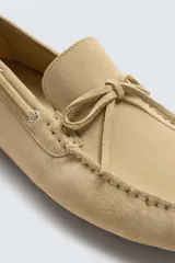 Mocasín casual de cuero color marrón claro con acabado serraje, horma redonda, detalle de lazo en el empeine y suela de goma.