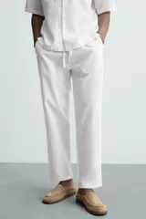 Pantalón de corte relajado color beige confeccionado en tejido de mezcla de algodón y lino. Posee cintura elástica ajustable con cordón, bolsillos frontales y bolsillos traseros de vivo.