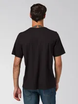 Remera de algodón de corte clásico y cuello redondo, color negro. Presenta un diseño minimalista con un pequeño gráfico bordado en el pecho y un parche de la marca en la manga izquierda.