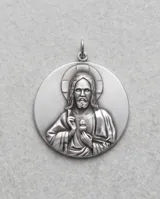 Collar triple de plata con cadenas finas de eslabones. El diseño incluye una cadena superior con un pequeño cilindro, una intermedia con una cuenta esférica y una inferior con un dije circular grabado con la imagen del Sagrado Corazón.
