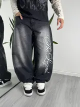 Jeans baggy de denim color negro con efecto acid wash, corte amplio tipo balloon fit y bordado cursivo con la frase "The Legend" en la pierna izquierda.