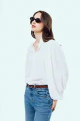 Camisa blanca de manga larga abullonada, con cuello alto y volados delicados en el borde.