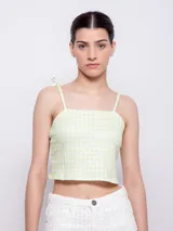 Top corto sin mangas, color verde lima y blanco, con estampado a cuadros vichy. Presenta tirantes finos que se atan en los hombros y escote cuadrado.