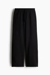 Pantalón tipo jogger de felpa color negro, con cintura elástica ajustable mediante cordón. Presenta un corte amplio y recto en las piernas, con bolsillos laterales discretos.
