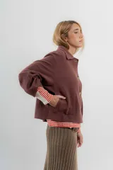 Chaqueta corta tipo blazer color marrón, confeccionada en tela de lana afieltrada. Tiene cuello camisero, silueta cuadrada, cierre frontal con botones y bolsillos delanteros.