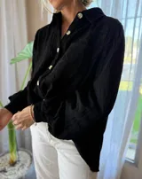 Camisa de manga larga confeccionada en muselina negra, con cuello clásico y cierre frontal de botones. Presenta un delicado bordado floral a tono sobre el hombro y bolsillo frontal.