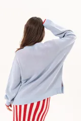 Buzo de punto color celeste con cuello redondo y diseño frontal de un velero tejido en tonos rojos y blancos, con detalles bordados a mano.