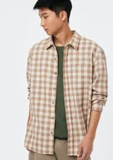 Camisa de manga larga con estampado a cuadros en tonos marrón y blanco, con cuello camisero, cierre frontal de botones y un bolsillo aplicado en el pecho.