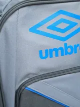 Mochila negra marca Umbro, con logo blanco en el frente y estampado de logos en relieve en la parte inferior. Cuenta con un bolsillo lateral de malla para botella y cierres con tiradores blancos.