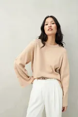Sweater de tejido liso color beige claro, con cuello redondo y mangas largas acampanadas que presentan una hilera de botones a tono en el lateral.