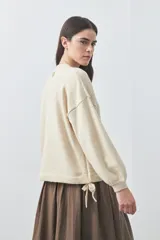 Sweater de tejido liviano con silueta relajada, hombros caídos y mangas largas con puños ajustados. Presenta cuello redondo y lazos ajustables en el bajo.