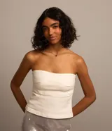 Blusa strapless de sarga color blanco hueso, de corte cropped y diseño ajustado con costuras visibles y cierre de cremallera lateral.