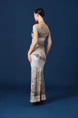 Vestido largo de corte ajustado con escote asimétrico tipo bote que deja un hombro al descubierto. Presenta un estampado artístico de paisaje en tonos neutros, tierra y gris sobre fondo claro, con un sutil fruncido en la zona de la cintura.