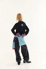 Sweater de punto color marrón con detalles en rojo en el cuello y los puños. Presenta un diseño de doble capa en el cuello y mangas largas con orificios para los pulgares, además de un pequeño bordado en el pecho y un acabado desflecado en el ruedo.