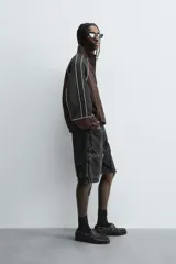 Cazadora de ajuste relajado, color marrón oscuro con bloques de color negro en las mangas. Presenta ribetes blancos que delinean los paneles y cuello alto con cierre frontal de cremallera. Los puños y el bajo son elásticos.