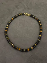 Collar corto de piedras volcánicas negras en la base del cuello, con pequeños detalles en tonos tostados y dorados.