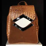 Mochila de cuero vacuno color marrón con estampado de cocodrilo en la parte superior y gamuza marrón en la parte inferior. Tiene detalles geométricos en charol negro y cuero blanco.