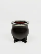 Mate de cerámica forrado en cuero color negro con aro de metal plateado en el borde superior. Tiene tres pequeñas patas de apoyo.