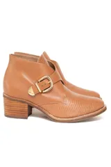 Bota corta de cuero vacuno grabado con efecto croco y terminación charolada en color ámbar. Presenta un diseño con hebilla metálica dorada lateral y taco medio fachetado con efecto madera.