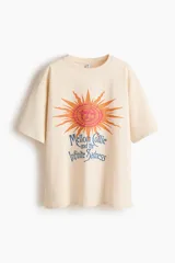 Remera oversized de algodón color beige con cuello redondo y hombros caídos. Presenta un gran estampado frontal en tonos naranja y azul con la inscripción "Mellon Collie and the Infinite Sadness" y un diseño de sol.
