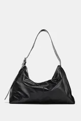 Bolso tipo saca de gran tamaño, color negro, con asa de hombro ajustable decorada con ojales metálicos y cierre principal mediante cremallera.