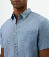 Camisa de manga corta confeccionada en mezcla de lino y algodón, con cuello inglés, cierre frontal de botones y bolsillo en el pecho. Presenta un corte comfort holgado y diseño liso.