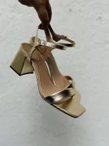 Sandalias doradas con tiras finas, punta cuadrada, talón abierto y hebilla ajustable en el tobillo. Taco bajo y ancho.