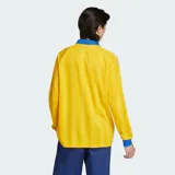 Camiseta de manga larga Adidas Originals, de corte holgado y color amarillo con rayas verticales sutiles en tono más oscuro y detalles en azul en cuello polo, puños y las clásicas franjas en las mangas. Cuenta con el logo bordado en el pecho.