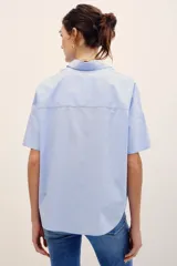 Camisa de manga corta celeste con rayas finas blancas, cuello camisero, cierre frontal con botones y corte amplio.