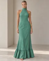 Vestido largo verde con cuello alto tipo halter, sin mangas y diseño ajustado con vuelo y volado en el dobladillo inferior.