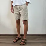 Bermuda de corte recto en color beige, confeccionada en tejido simil lino. Presenta cintura elástica con cordón de ajuste y bolsillos laterales.