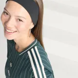 Camiseta de punto oversized verde oscuro de la colección Icons de Adidas, inspirada en los años 80, con rayas diplomáticas blancas, las icónicas tres tiras de la marca en las mangas, cuello redondo y el logotipo del trébol bordado junto al escudo vintage de la Juventus.