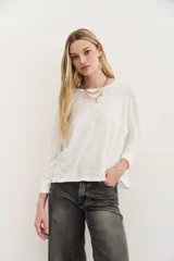 Remera blanca de algodón peruano con textura jaspeada, de moldería holgada, cuello redondo y mangas largas que se ajustan en la muñeca.