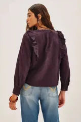 Camisa blanca de algodón con diseño romántico, cuello alto con volados, cierre frontal de botones y detalles de encaje y bordados calados. Presenta mangas largas con puños de encaje y volados frontales.