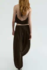 Pantalón baggy de satén color marrón, con cintura elástica y bajos ajustados con elástico, creando un efecto de volumen en las piernas.