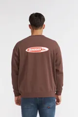 Buzo Quiksilver color marrón, con cuello redondo, mangas largas y el pequeño logotipo de la marca estampado en el centro del pecho dentro de un óvalo rojo con borde blanco.